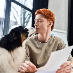 A dog nuzzling a young man's face while he reviews planned giving paperwork, reflecting the lasting bond between people and pets at the Humane Society of Catawba County